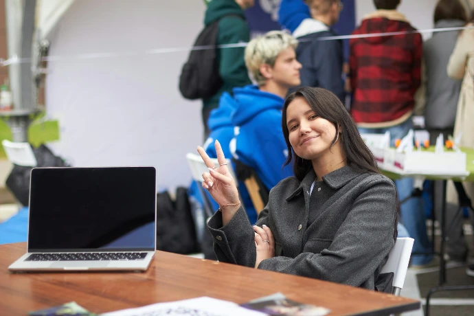 A smiling woman holds up two fingers near a laptop.